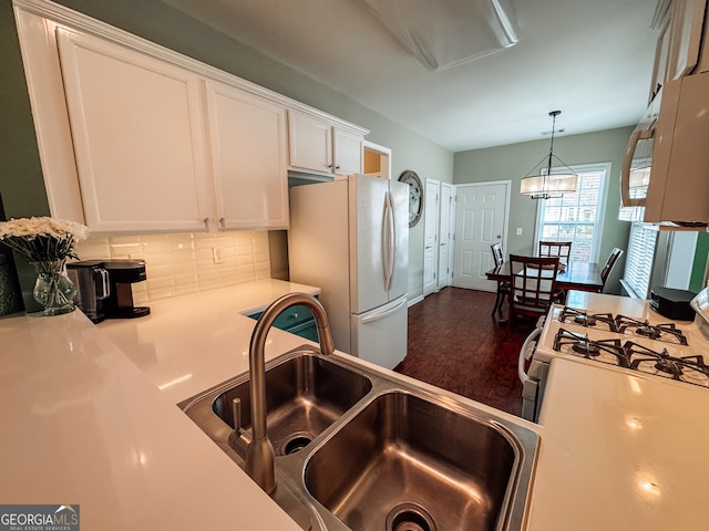 kitchen featuring white appliances, white cabinets, hanging light fixtures, a sink, and backsplash