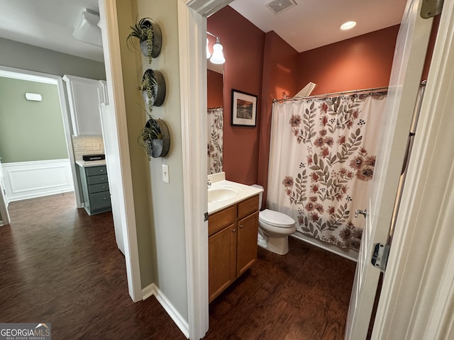 bathroom featuring visible vents, a decorative wall, toilet, vanity, and wood finished floors