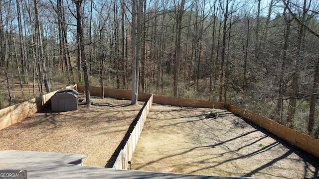 view of yard featuring a storage shed, an outdoor structure, a fenced backyard, and a forest view