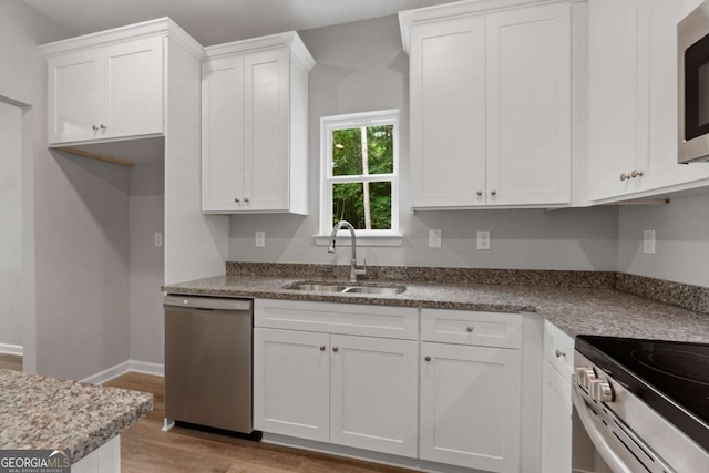 kitchen with appliances with stainless steel finishes, sink, white cabinets, and light hardwood / wood-style floors