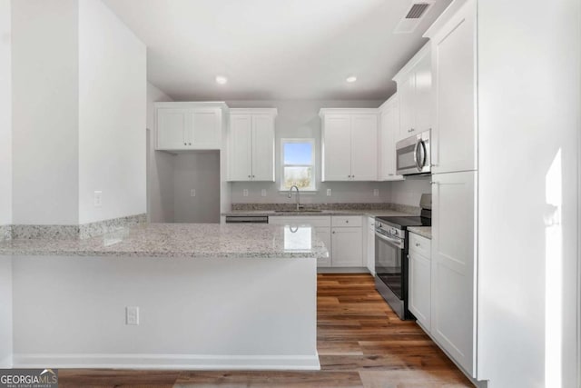 kitchen with white cabinetry, sink, hardwood / wood-style flooring, stainless steel appliances, and light stone countertops