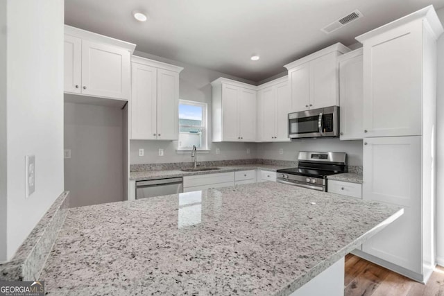 kitchen with sink, white cabinetry, light hardwood / wood-style flooring, appliances with stainless steel finishes, and light stone countertops