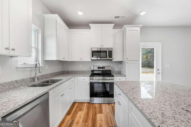 kitchen featuring sink, light stone counters, light hardwood / wood-style flooring, appliances with stainless steel finishes, and white cabinets