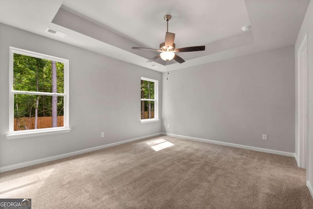 carpeted empty room with a raised ceiling and ceiling fan