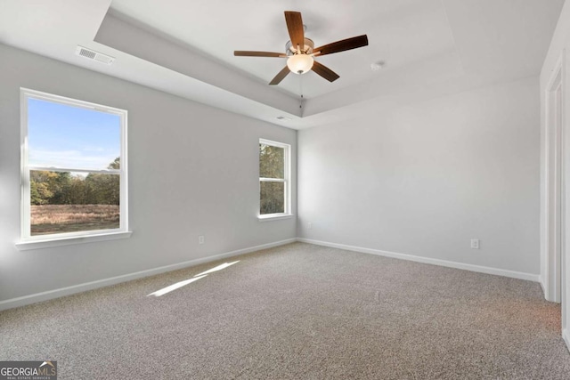 carpeted empty room featuring a tray ceiling, plenty of natural light, and ceiling fan