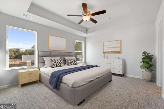 bedroom with carpet flooring, a tray ceiling, and multiple windows