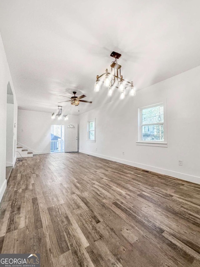 unfurnished living room featuring ceiling fan with notable chandelier, visible vents, baseboards, and wood finished floors