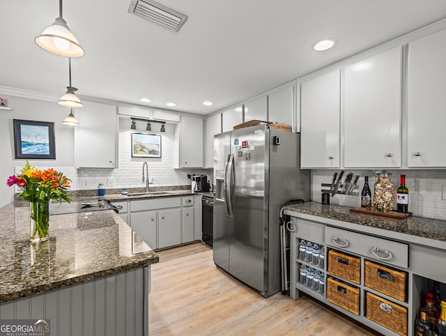 kitchen with sink, decorative light fixtures, stainless steel fridge, dark stone counters, and light hardwood / wood-style floors