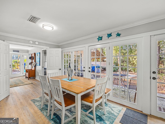 dining room with french doors, ornamental molding, and light wood-type flooring