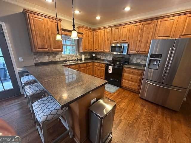 kitchen featuring a breakfast bar area, backsplash, stainless steel appliances, dark hardwood / wood-style flooring, and decorative light fixtures