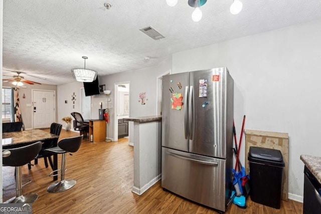 kitchen with stainless steel fridge, hanging light fixtures, black dishwasher, a textured ceiling, and light wood-type flooring