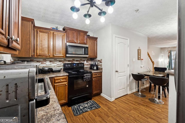 kitchen featuring black electric range oven, backsplash, a chandelier, light stone counters, and light hardwood / wood-style flooring