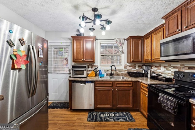 kitchen with tasteful backsplash, sink, stainless steel appliances, light stone countertops, and light hardwood / wood-style flooring