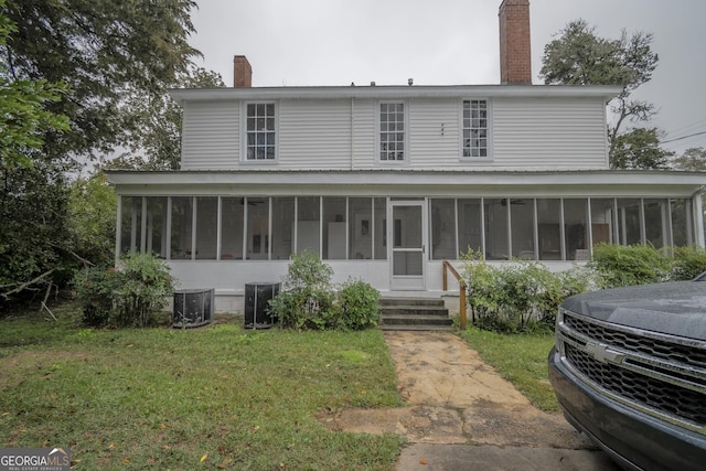 back of property featuring central AC unit, a sunroom, and a lawn