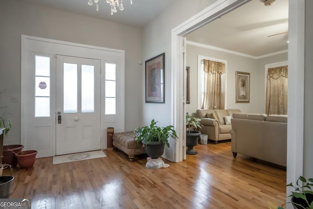 foyer with crown molding, an inviting chandelier, and light wood-type flooring