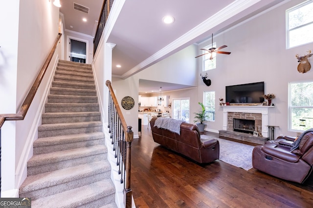 living room featuring dark wood-type flooring, ceiling fan, a high ceiling, a fireplace, and ornamental molding