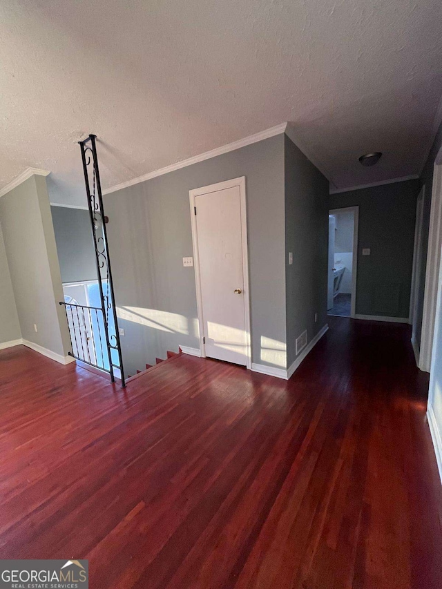 empty room with crown molding, dark wood-type flooring, and a textured ceiling