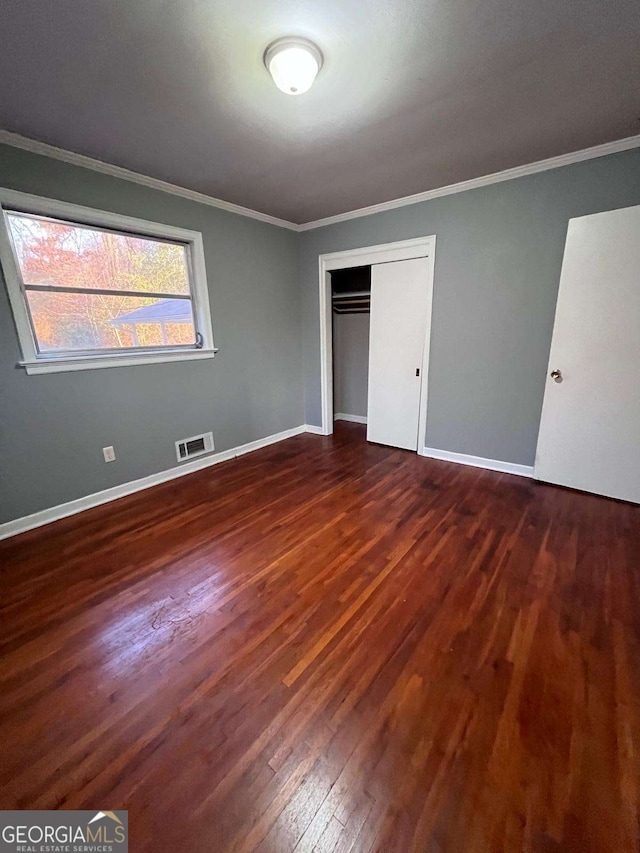 unfurnished bedroom with dark wood-type flooring, ornamental molding, and a closet