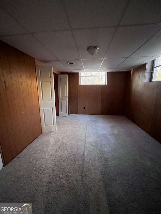 basement with carpet, a paneled ceiling, and wooden walls