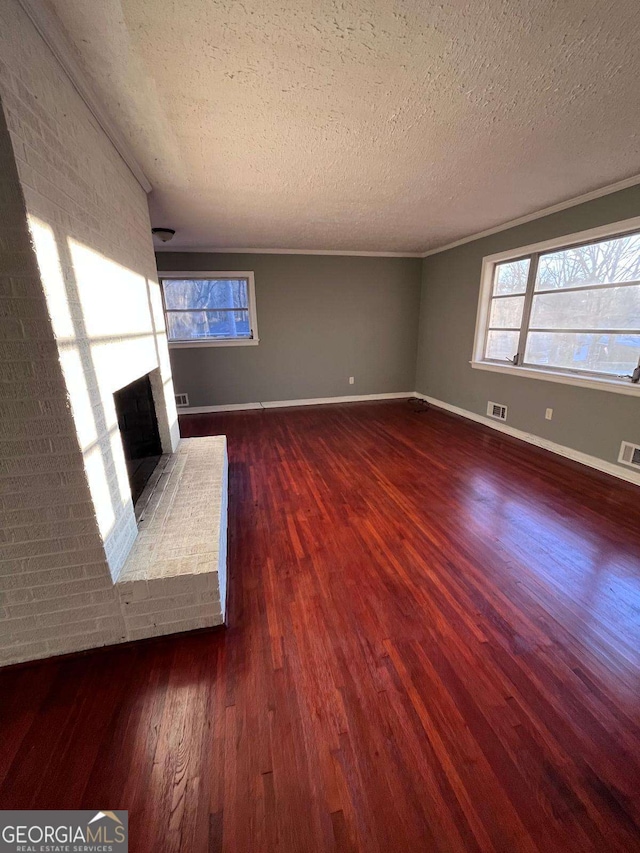 unfurnished living room with ornamental molding, a brick fireplace, dark wood-type flooring, and a textured ceiling