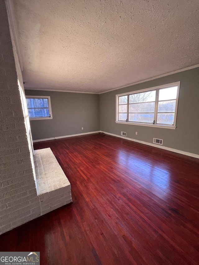 interior space featuring dark wood-type flooring, ornamental molding, a textured ceiling, and a wealth of natural light