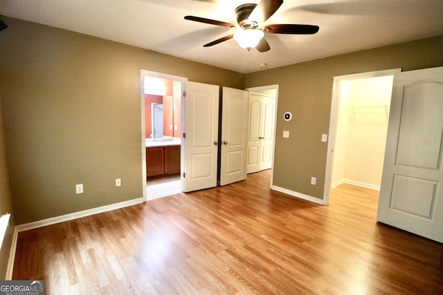 unfurnished bedroom with light hardwood / wood-style flooring, ceiling fan, connected bathroom, a walk in closet, and a closet