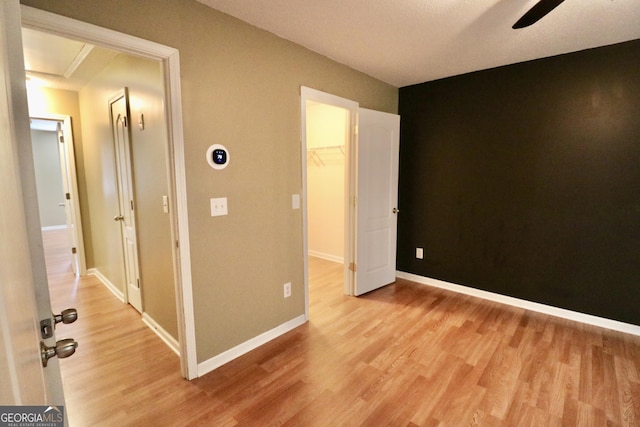 unfurnished bedroom with a spacious closet, light hardwood / wood-style floors, a closet, and ceiling fan