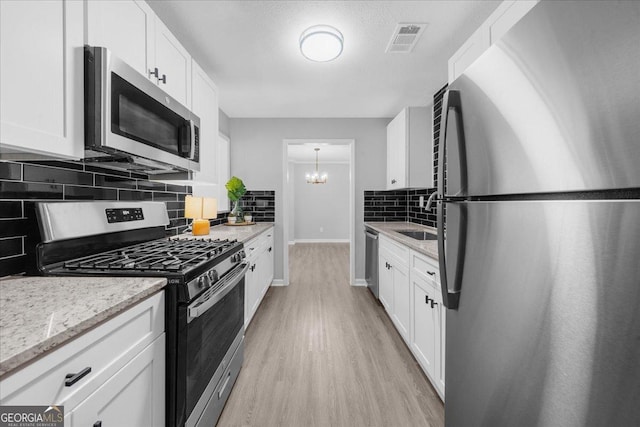 kitchen with sink, appliances with stainless steel finishes, light stone counters, white cabinets, and light wood-type flooring