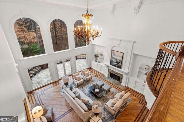 living room featuring a towering ceiling, built in features, a chandelier, a premium fireplace, and light wood-type flooring