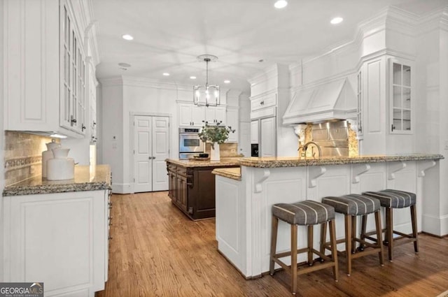 kitchen with white cabinetry, decorative light fixtures, custom exhaust hood, and kitchen peninsula