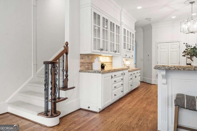 interior space featuring decorative light fixtures, white cabinets, decorative backsplash, light hardwood / wood-style floors, and crown molding