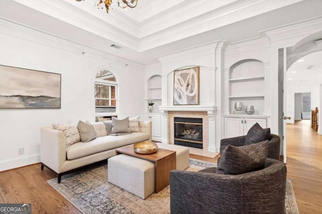 living room with crown molding, built in features, a chandelier, and light wood-type flooring