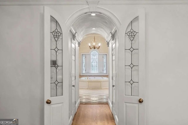 hall featuring vaulted ceiling, crown molding, a chandelier, and hardwood / wood-style floors