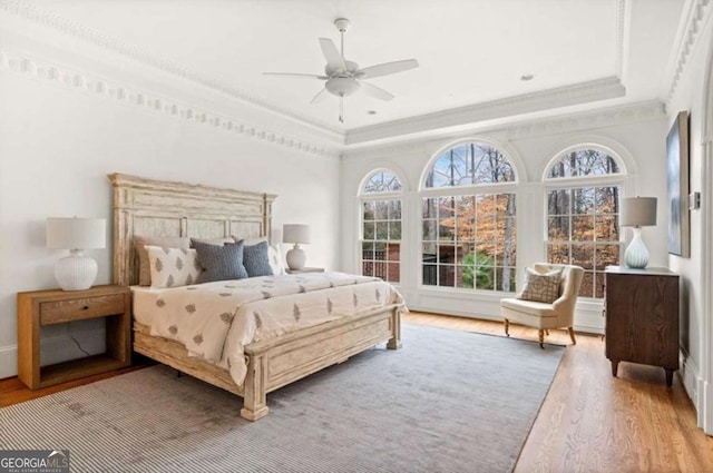 bedroom with a tray ceiling, hardwood / wood-style flooring, crown molding, and ceiling fan