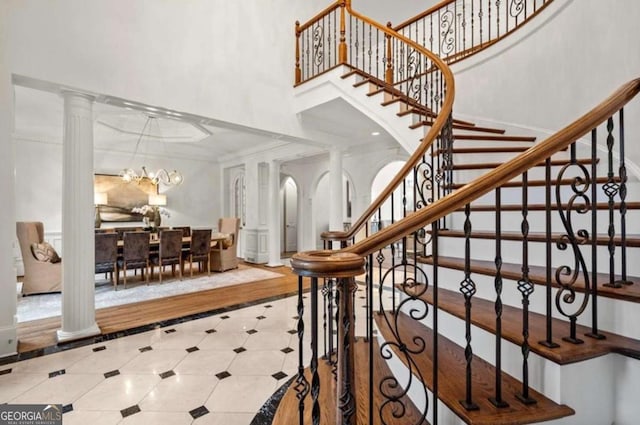 staircase featuring ornate columns, crown molding, a towering ceiling, and a notable chandelier