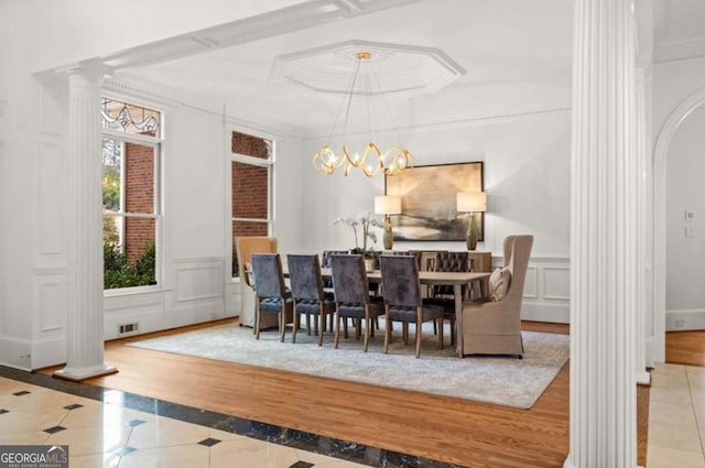 tiled dining area with decorative columns, crown molding, a raised ceiling, and a notable chandelier