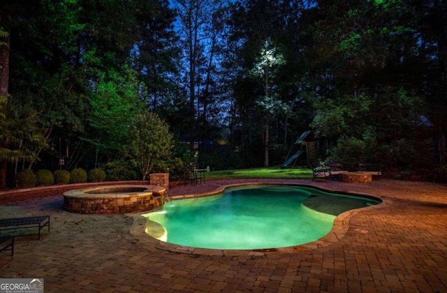 pool at night featuring a patio area and an in ground hot tub