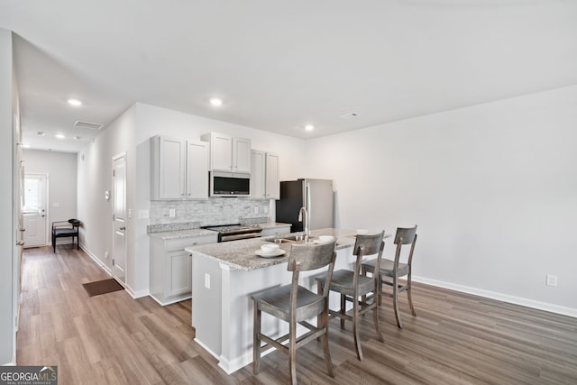 kitchen with a breakfast bar, light stone counters, stainless steel appliances, an island with sink, and decorative backsplash