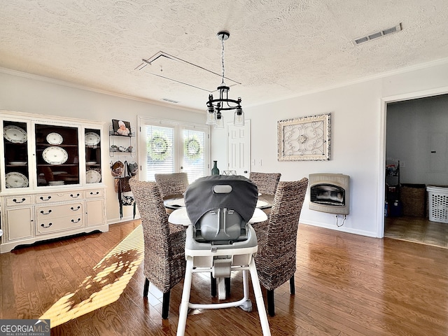 dining space featuring heating unit, an inviting chandelier, ornamental molding, a textured ceiling, and hardwood / wood-style floors