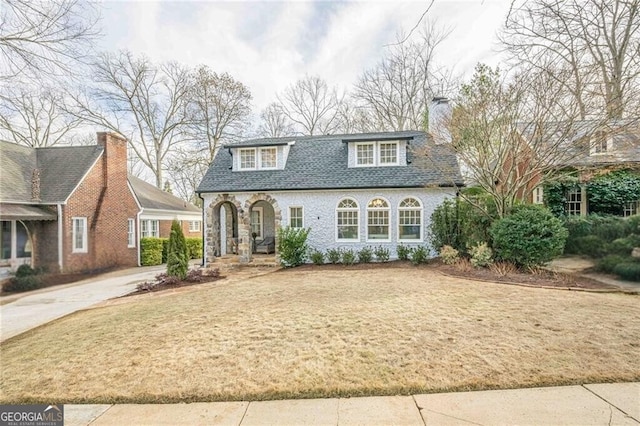 view of front facade with a shingled roof, a chimney, concrete driveway, and a front yard