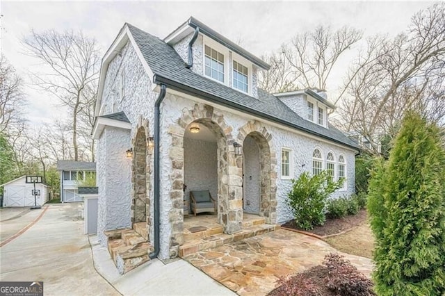 view of front of house with stone siding, roof with shingles, and an outdoor structure