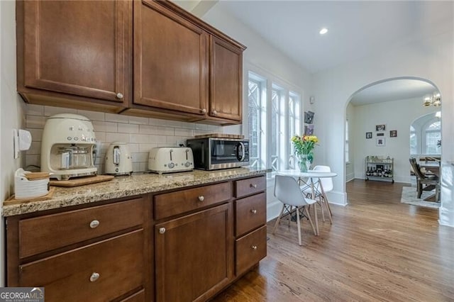 kitchen with tasteful backsplash, light stone countertops, and light wood-type flooring