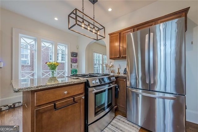 kitchen featuring light stone counters, hanging light fixtures, stainless steel appliances, and light hardwood / wood-style floors