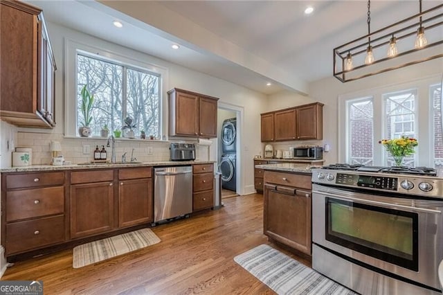 kitchen featuring appliances with stainless steel finishes, decorative light fixtures, sink, decorative backsplash, and stacked washer / drying machine