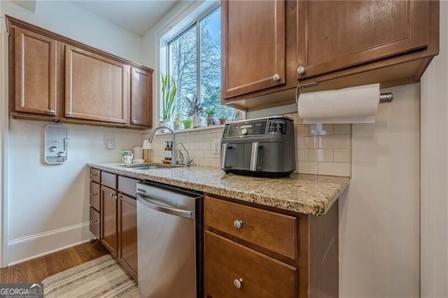 kitchen featuring light stone counters, dishwasher, sink, and decorative backsplash