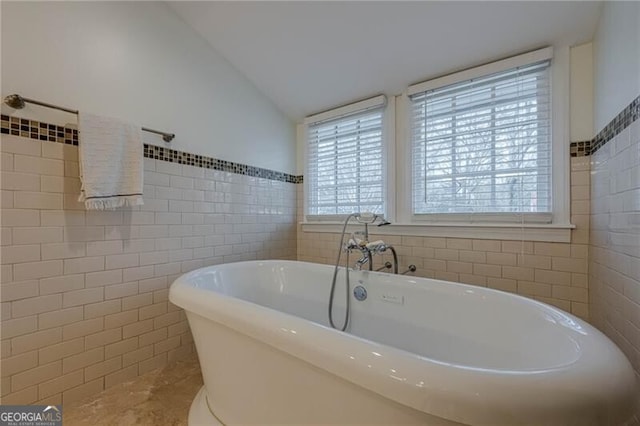 bathroom with a bath, vaulted ceiling, tile walls, and a wealth of natural light