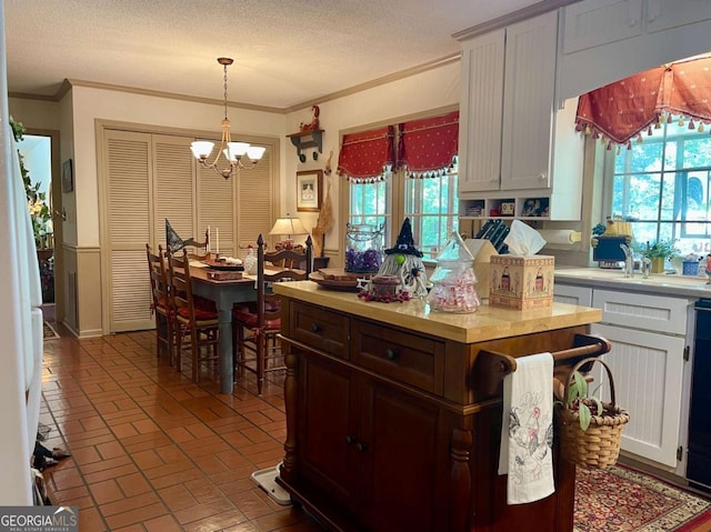 kitchen with hanging light fixtures, crown molding, a healthy amount of sunlight, and white cabinets