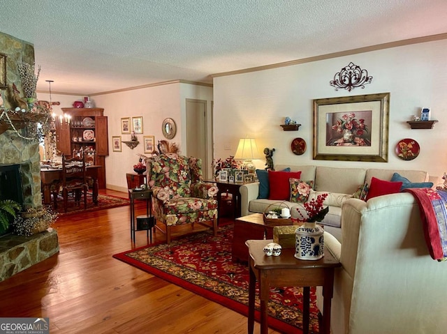 living room featuring a stone fireplace, crown molding, an inviting chandelier, wood-type flooring, and a textured ceiling