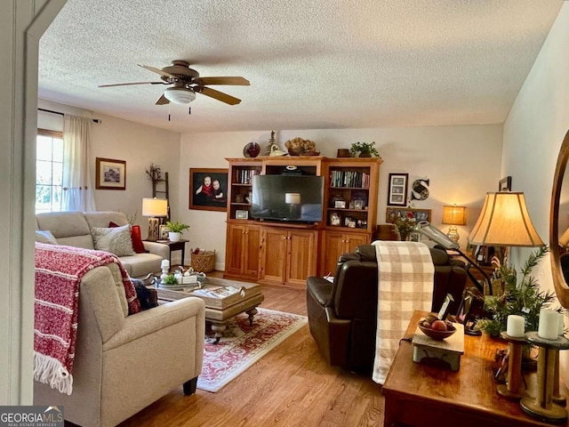 living room featuring ceiling fan, a textured ceiling, and light wood-type flooring