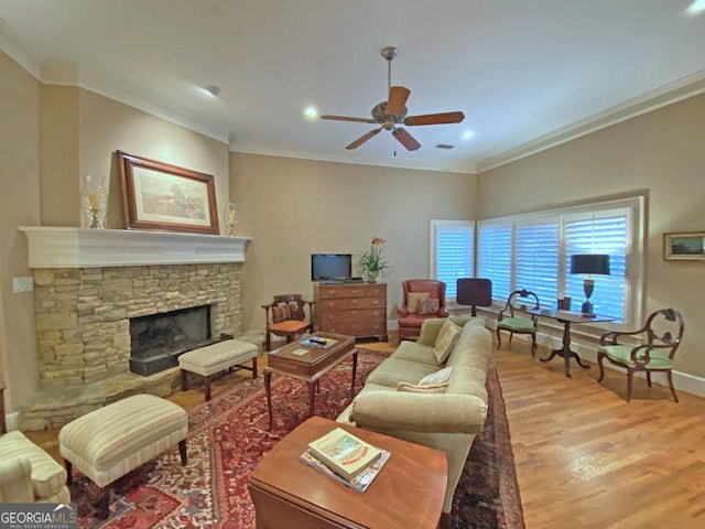 living room featuring crown molding, ceiling fan, a stone fireplace, and light hardwood / wood-style flooring